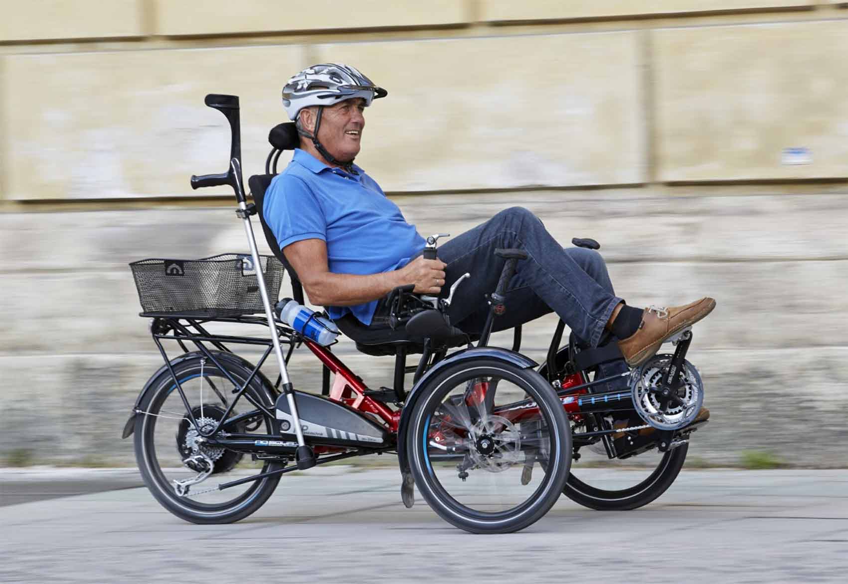 Alter Mann sitzt in einem Seniorendreirad und fährt an einer Mauer entlang